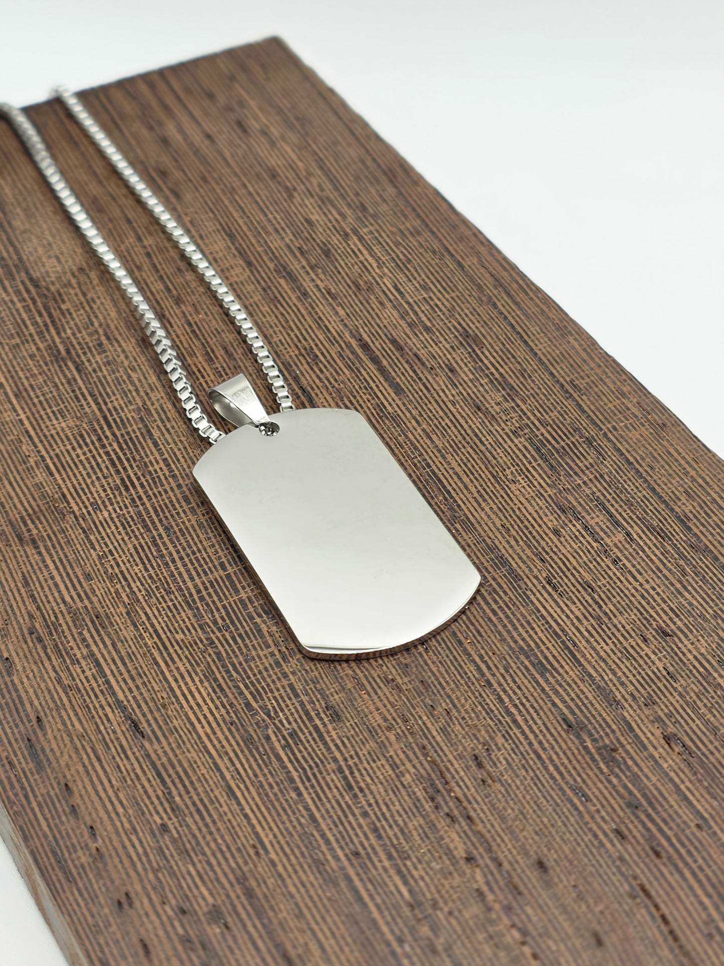 Silver dog tag pendant on a chain against a wooden background