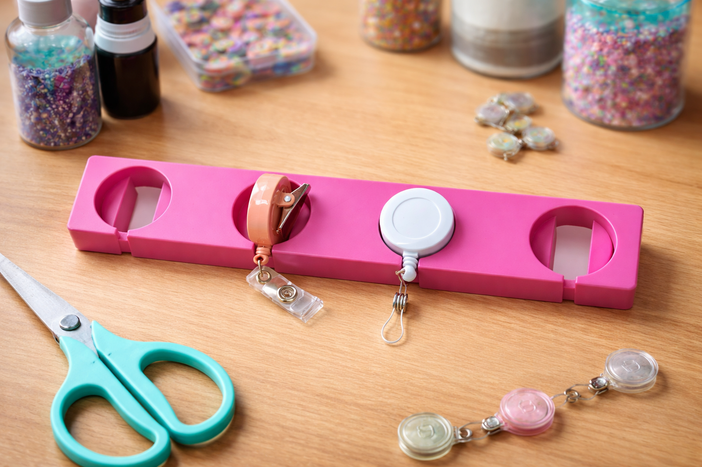 Pink holder with retractable badges on a wooden surface with craft supplies.