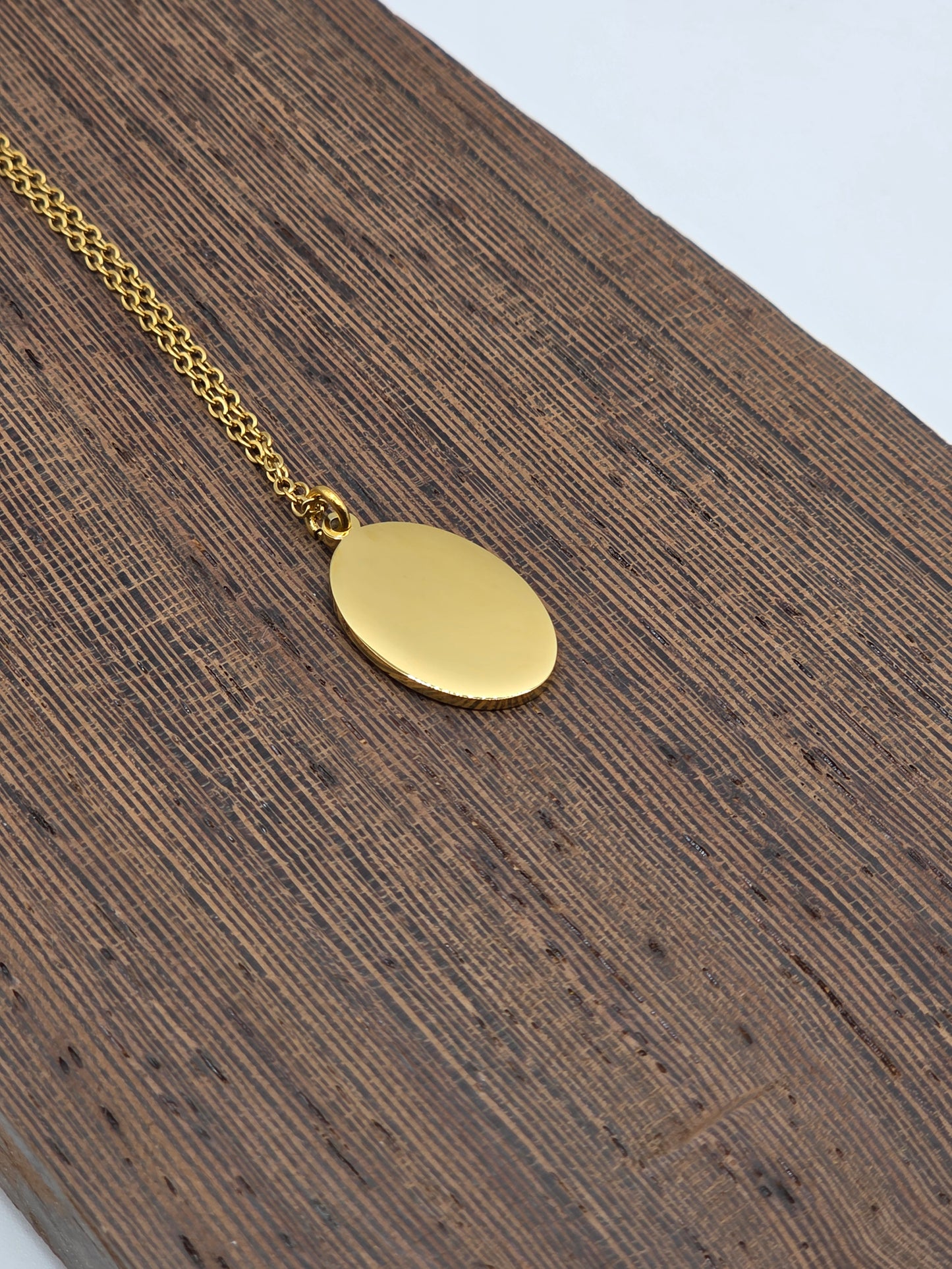 Gold necklace with an oval pendant on a wooden surface