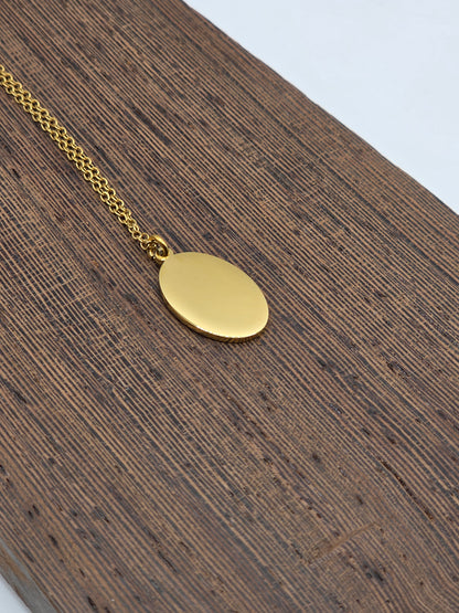 Gold necklace with an oval pendant on a wooden surface