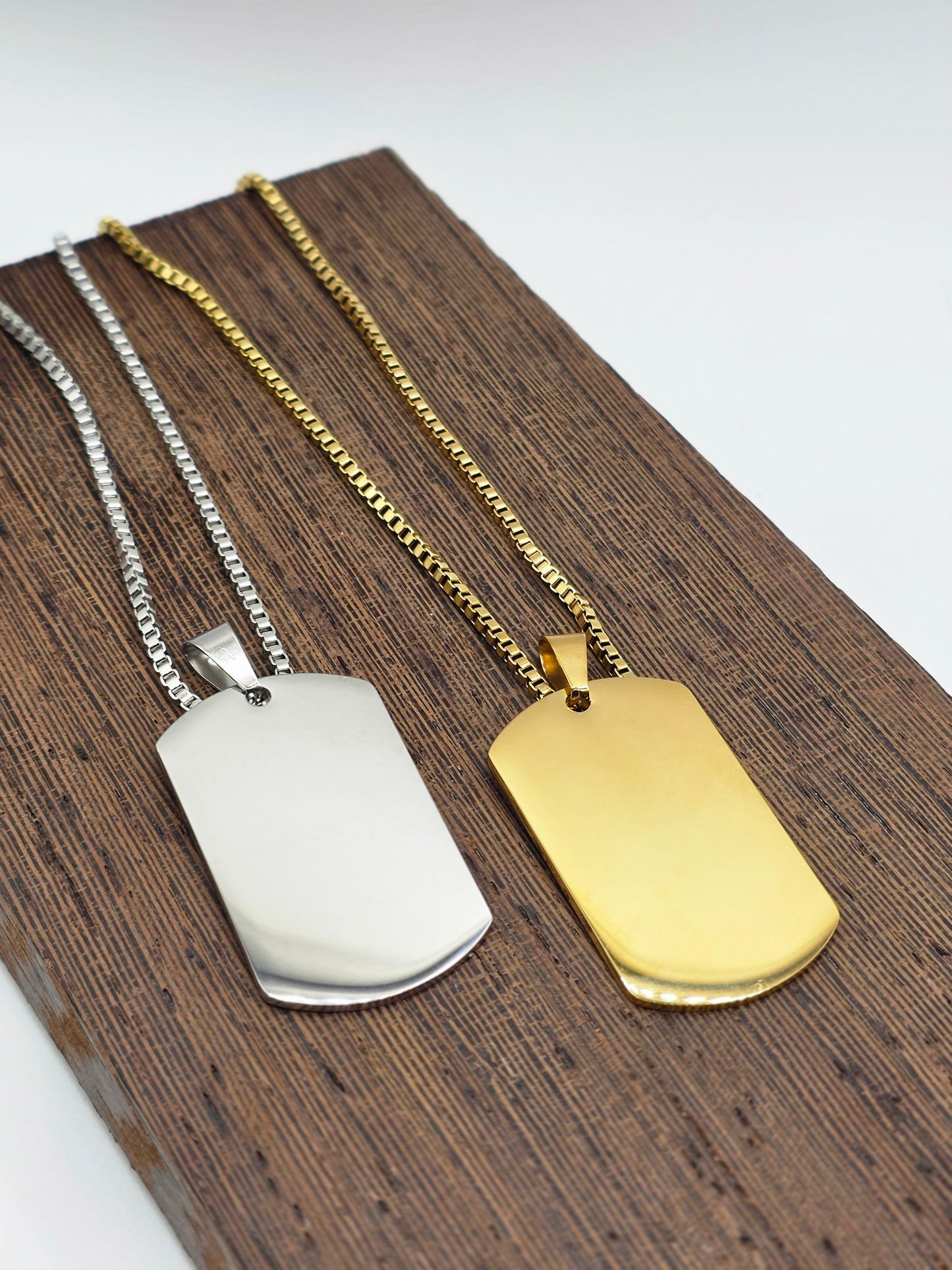 Two dog tags, one gold and one silver, on a wooden surface.
