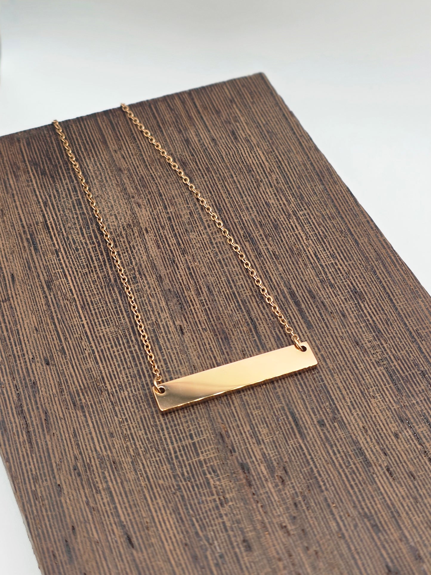 Rose Gold necklace with a bar pendant on a wooden surface