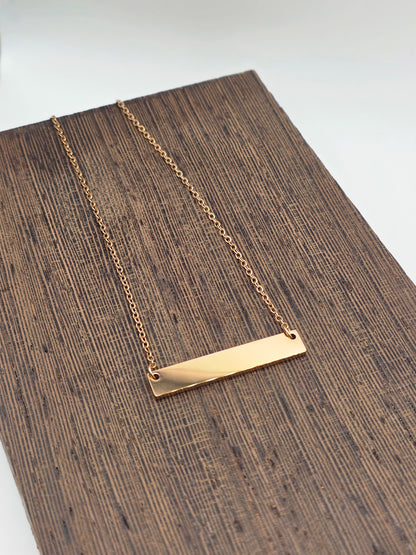 Rose Gold necklace with a bar pendant on a wooden surface