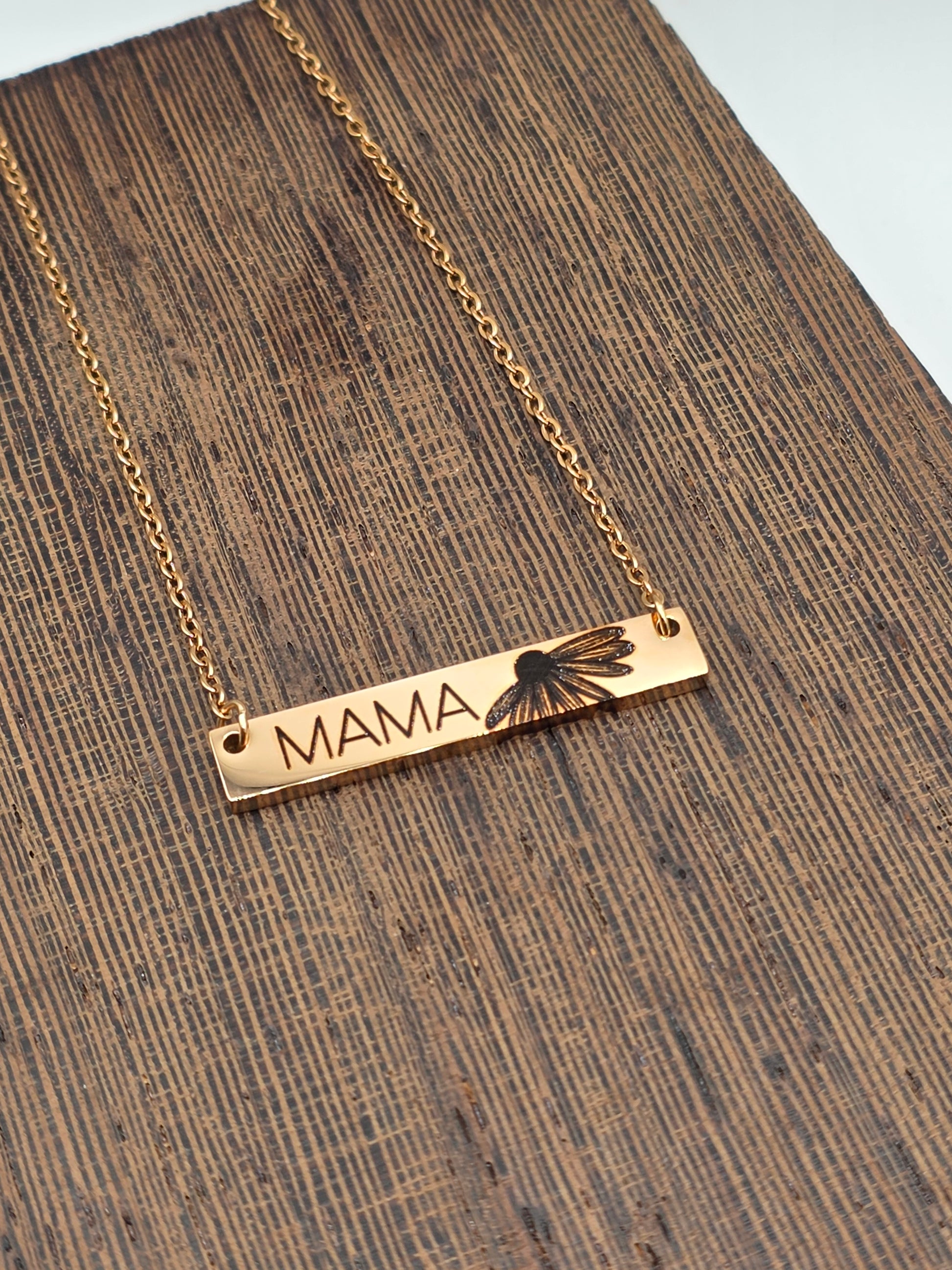 Gold necklace with a bar pendant on a wooden surface engraved with daisy and Mama