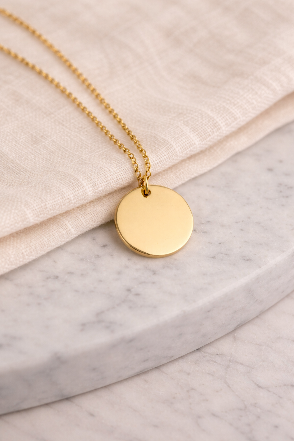 Gold necklace with a round pendant on a marble surface