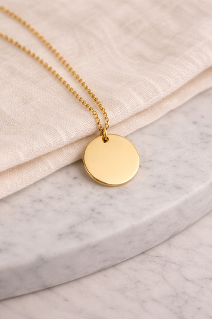 Gold necklace with a round pendant on a marble surface