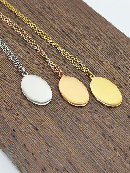 Three gold necklaces with oval pendants on a wooden surface