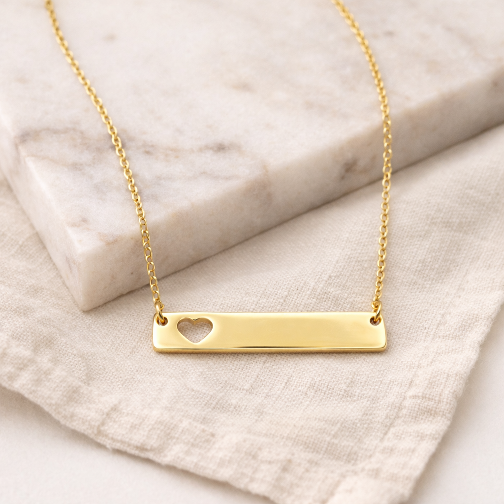 Gold necklace with a heart cutout on a marble surface