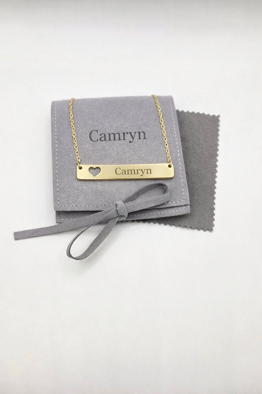 Gold necklace with 'Camryn' engraving on a gray jewelry pouch with a heart detail.