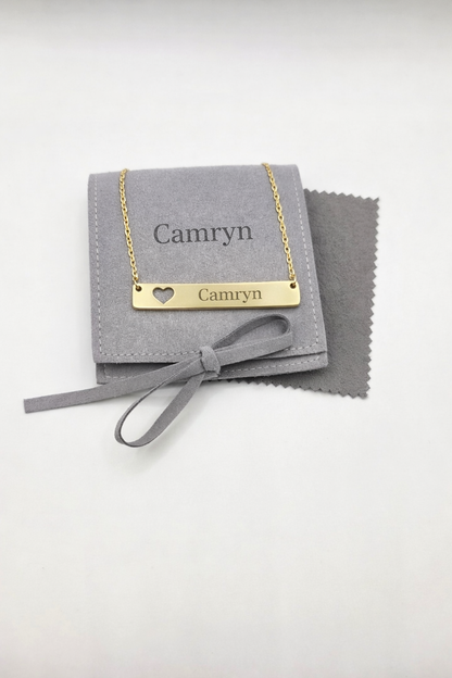 Gold necklace with 'Camryn' engraving on a gray jewelry pouch with a heart detail.