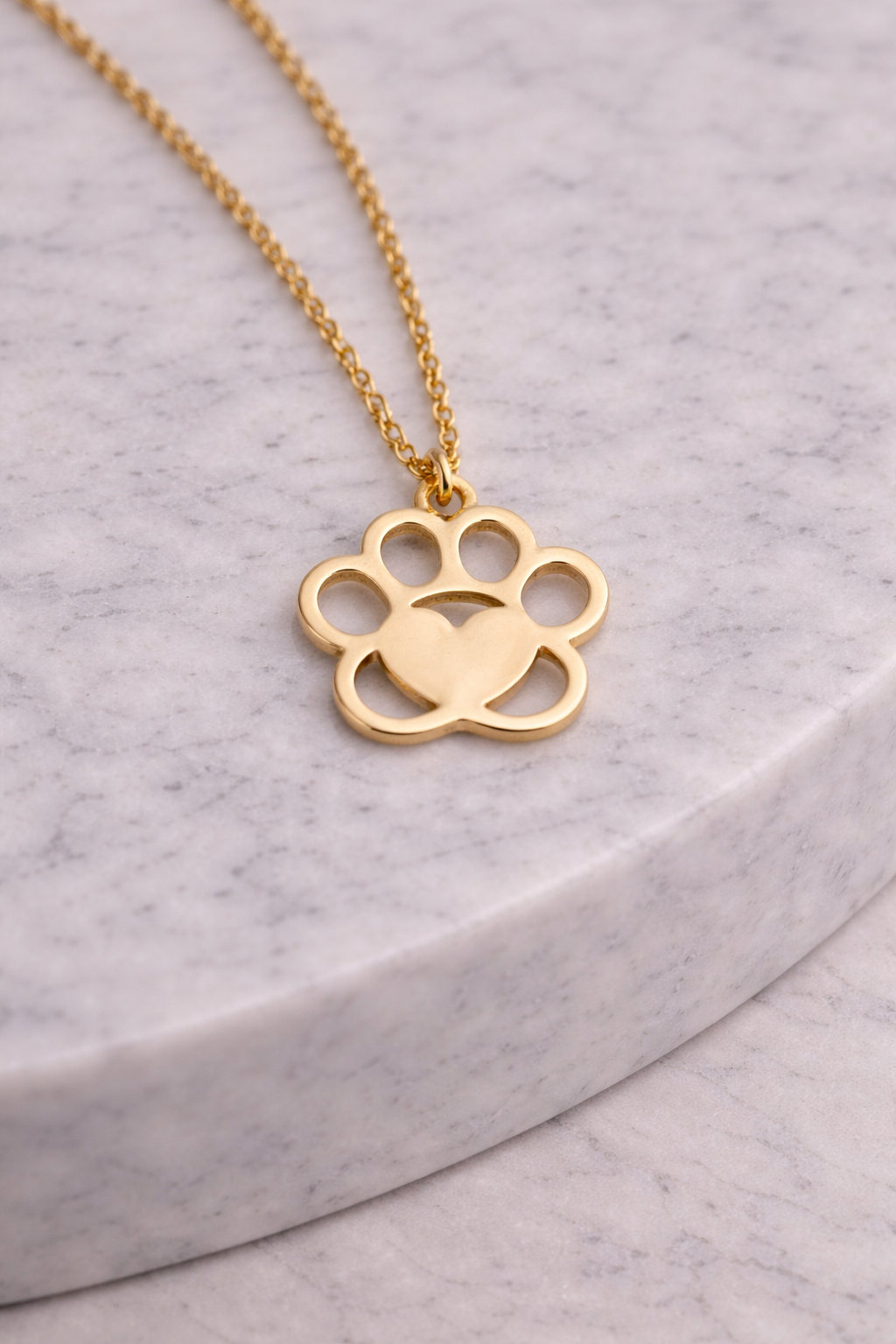 Gold paw print necklace on a gray surface