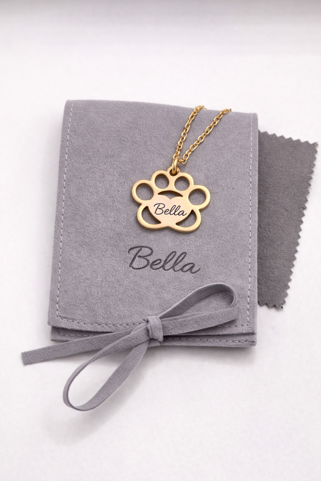 Gold paw-shaped necklace with 'Bella' engraving on a gray jewelry pouch.