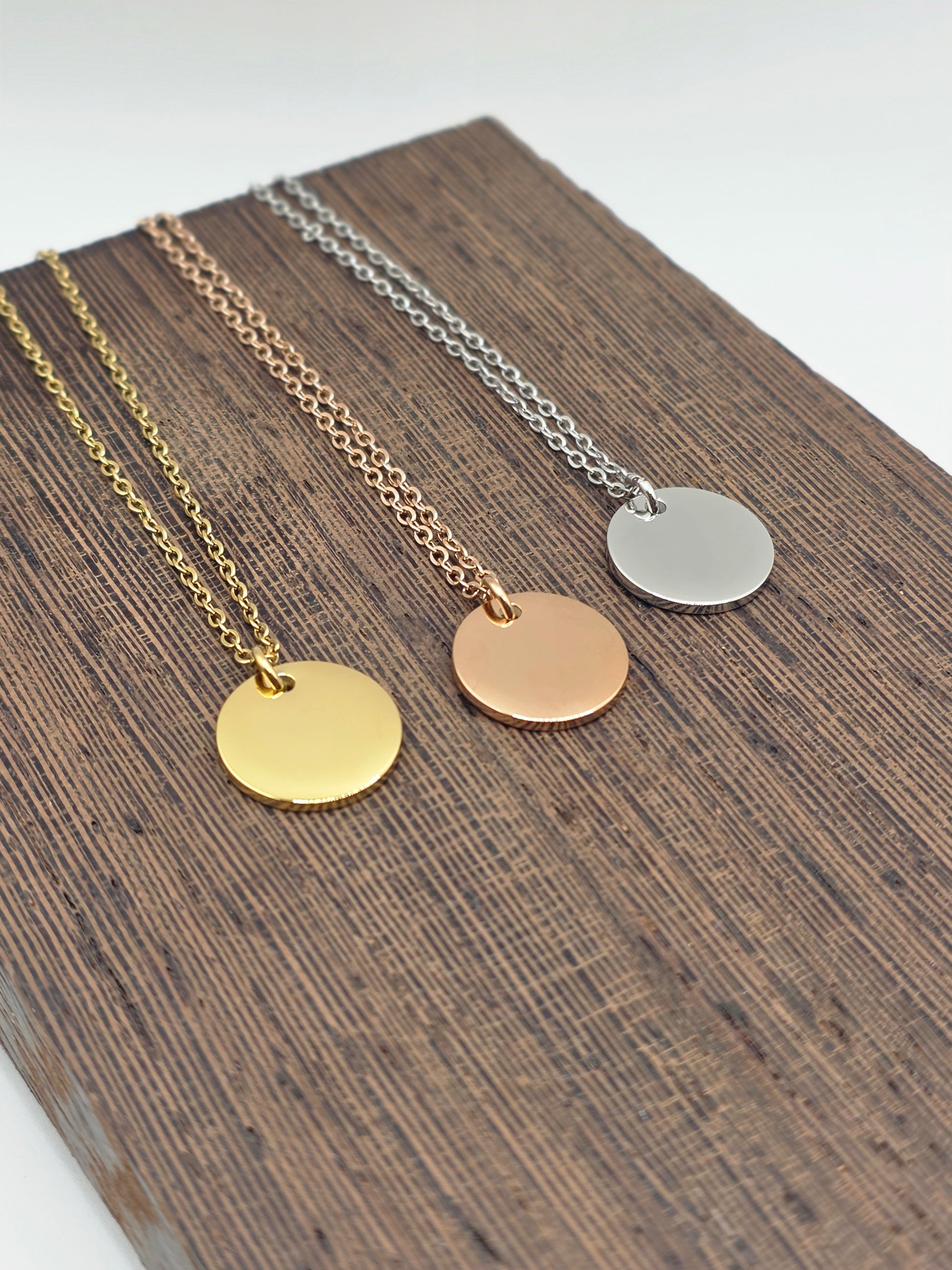 Three necklaces with round pendants in silver, gold, and rose gold on a wooden surface.