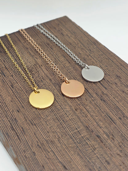 Three necklaces with round pendants in silver, gold, and rose gold on a wooden surface.